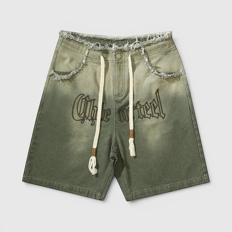 Calções Allzom de ganga verde com lavagem vintage, bordas desfiadas, cordão ajustável e bordado estilo gótico.