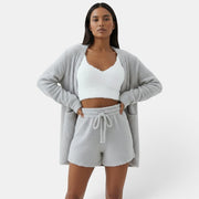 Mulher com conjunto de pijama Allzom de 3 peças em cinza, com top curto branco, tank e calções em tecido felpudo.