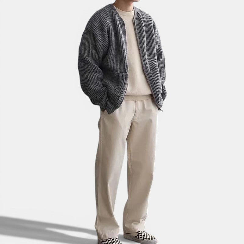 Allzom Men's grey knitted zip-up cardigan with funnel neck and pockets, worn over a cream sweater and beige trousers.