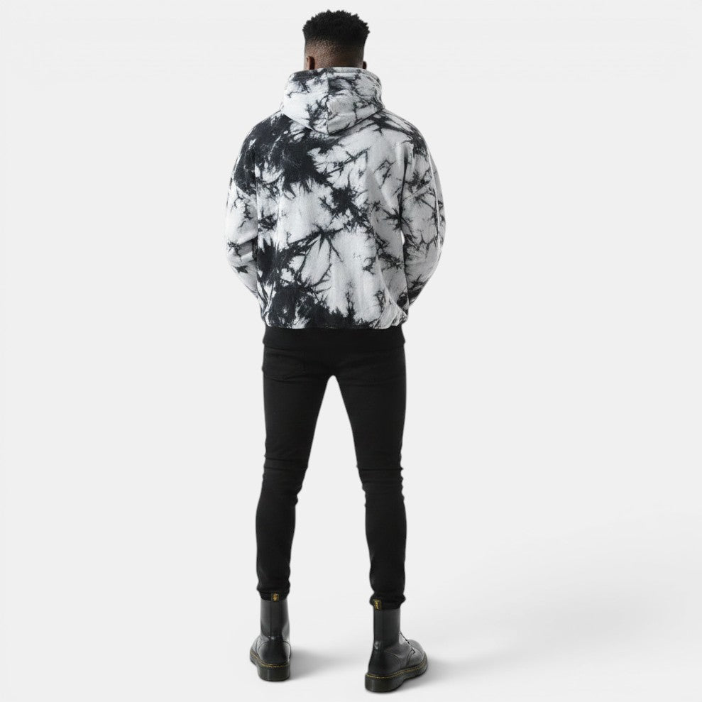 Allzom homem com capuz tie-dye preto e branco solto, calças pretas e botas pretas.
