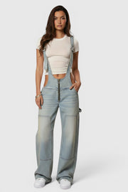 Jardineiras de ganga Allzom estilo Y2K com fecho frontal, corte largo e bolsos, usadas por modelo com t-shirt branca.