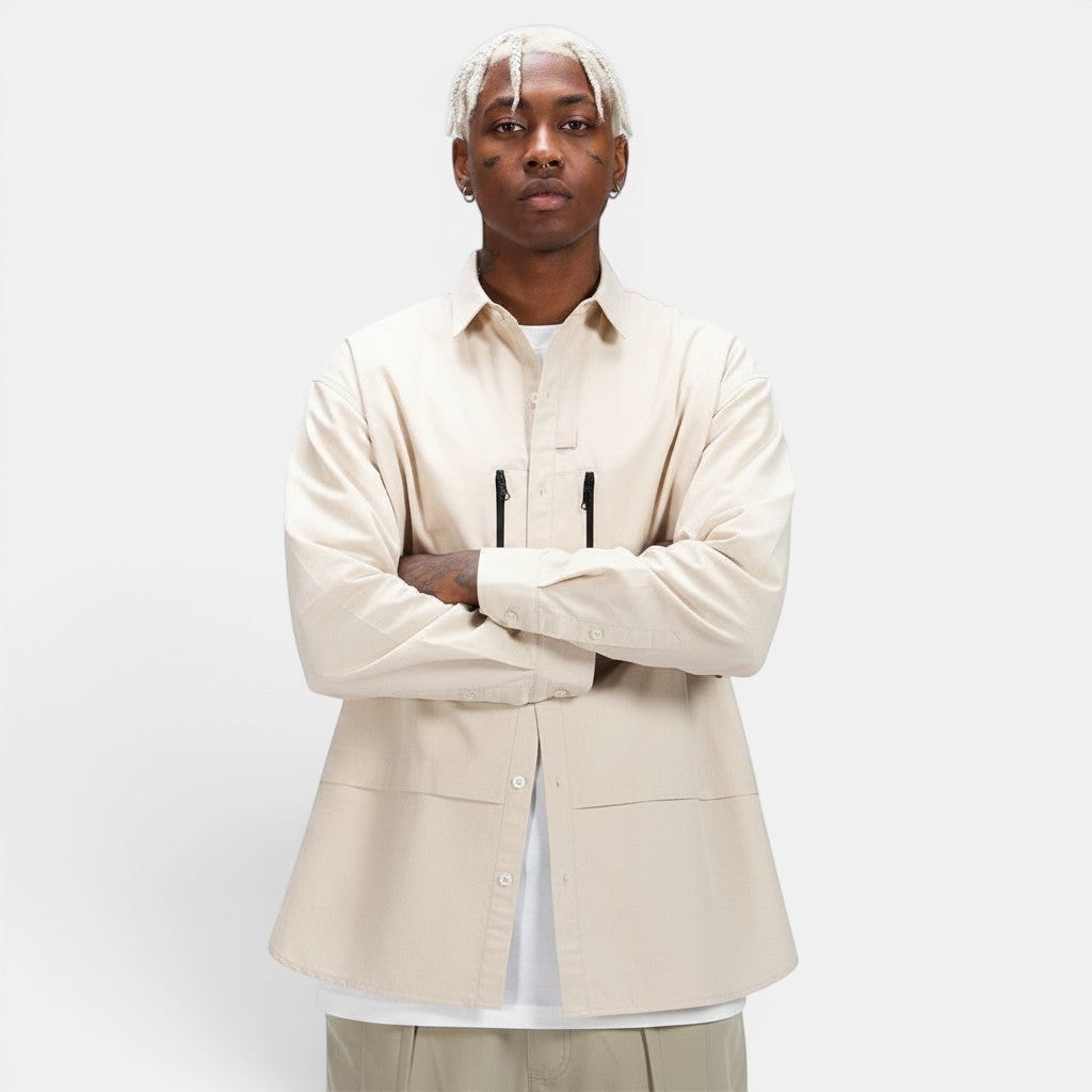 Allzom Men's beige long-sleeve shirt jacket with zipper pockets and button closure. Model is wearing it over a white t-shirt.