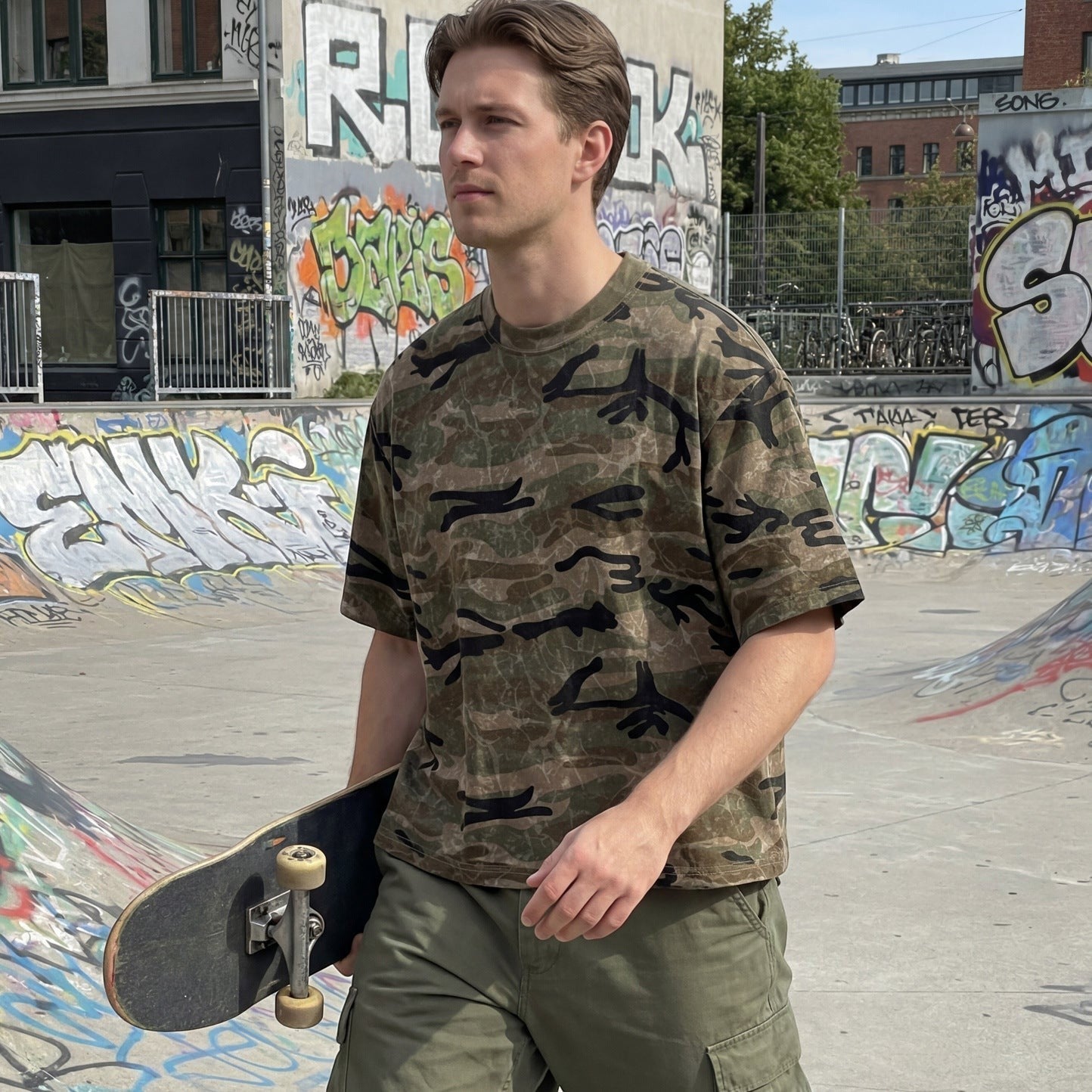Homem com t-shirt Allzom de algodão com padrão camuflado verde, corte descontraído e gola redonda num skatepark.