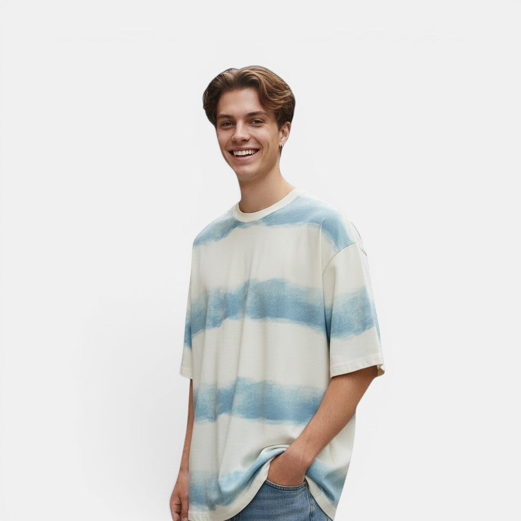 Allzom T-shirt de algodão branca com padrão de listras azuis em aquarela. Modelo masculino com as mãos nos bolsos.